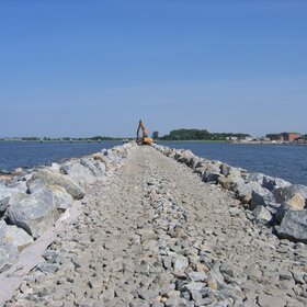 Steindamm im Wasser mit Baumaschine im Hintergrund